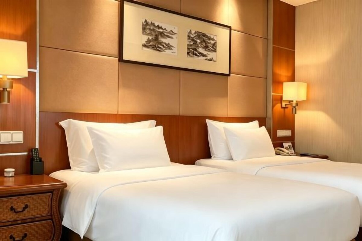 Ett hotellrum med två sängar, en sänggavel i trä, sänglampor och inramade konstverk på väggen.