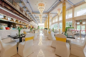 A spacious restaurant with high ceilings, chandeliers, and a long counter with a bar area.
