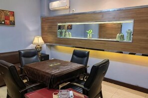 A hotel dining area with a table, chairs, a lamp, and a wall-mounted mirror.
