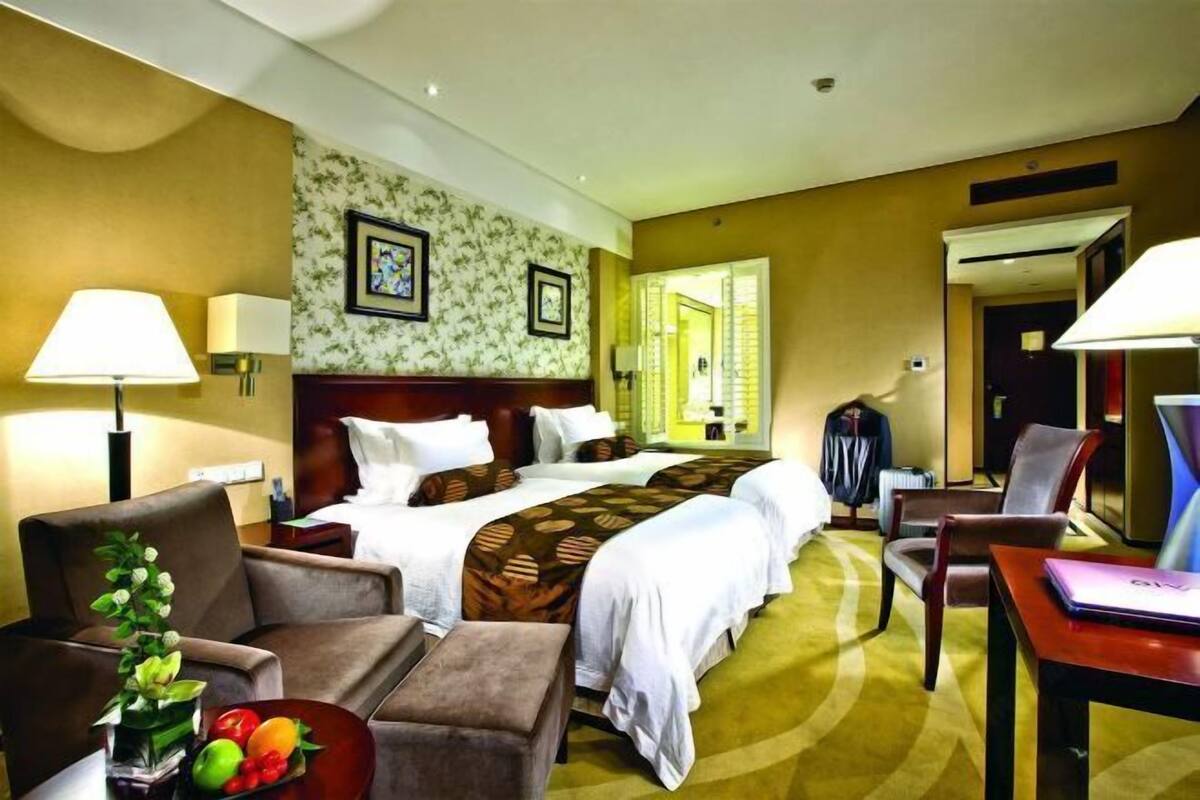 Une chambre d’hôtel avec un grand lit, deux tables de chevet, un bureau, une chaise et une petite table sur laquelle est posé un vase de fleurs.