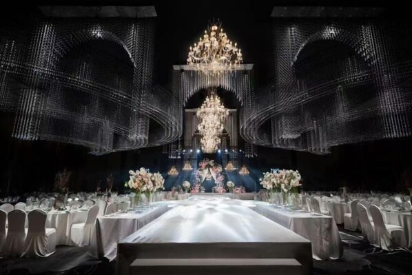 Une salle de banquet avec une longue table dressée pour un événement formel, entourée de chaises.