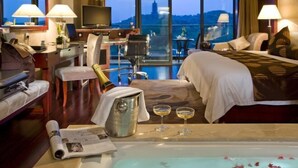 Een hotelkamer met een groot bed, een bureau met een computer, een televisie, een minibar en uitzicht op een berg.