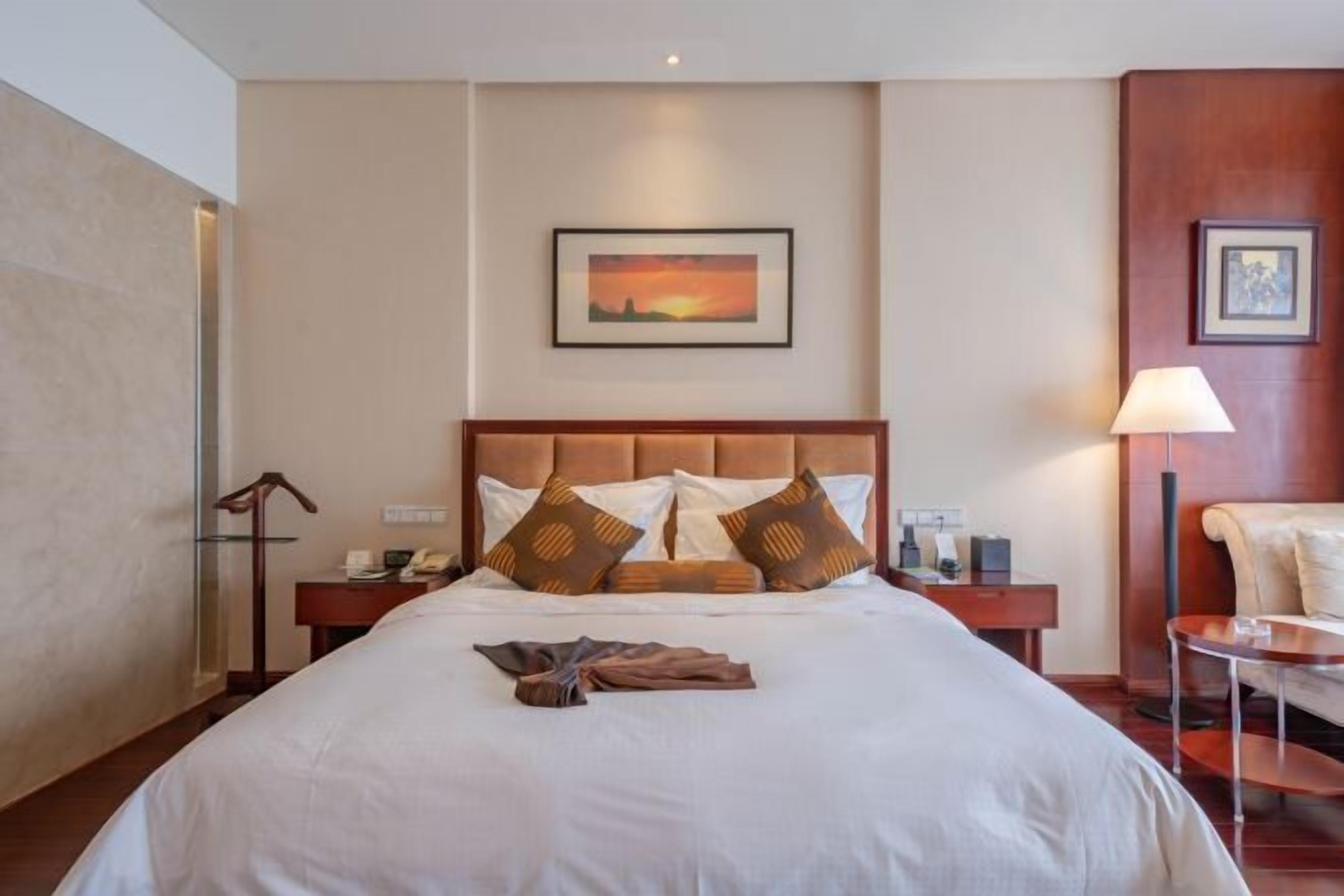 A hotel room with a large bed, a nightstand, a chair, and a painting on the wall.