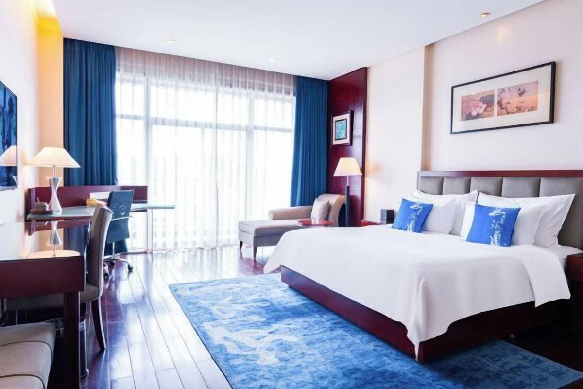 Une chambre d’hôtel avec un lit, un bureau, une chaise et une grande fenêtre.