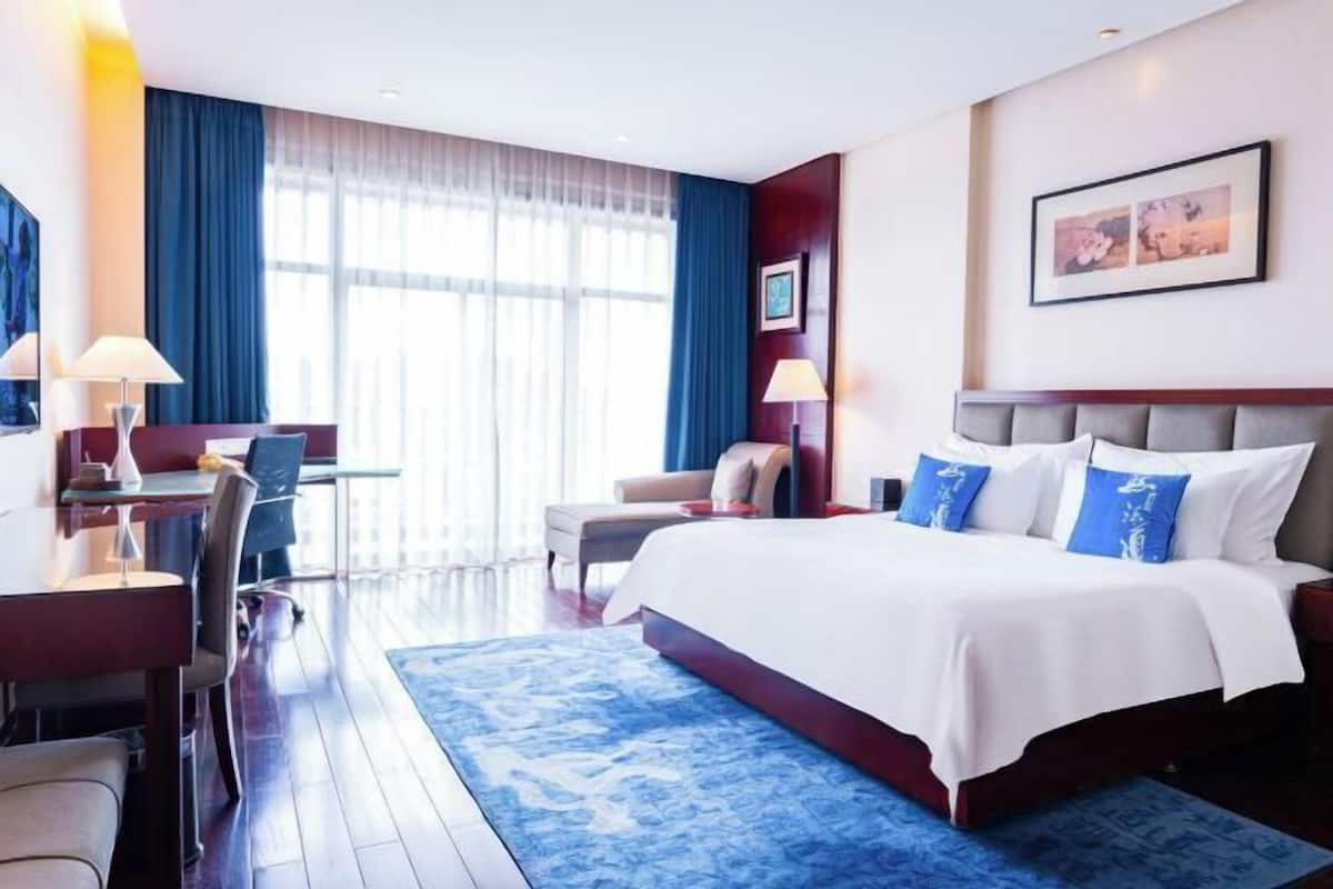A hotel room with a bed, desk, chair, and a large window.
