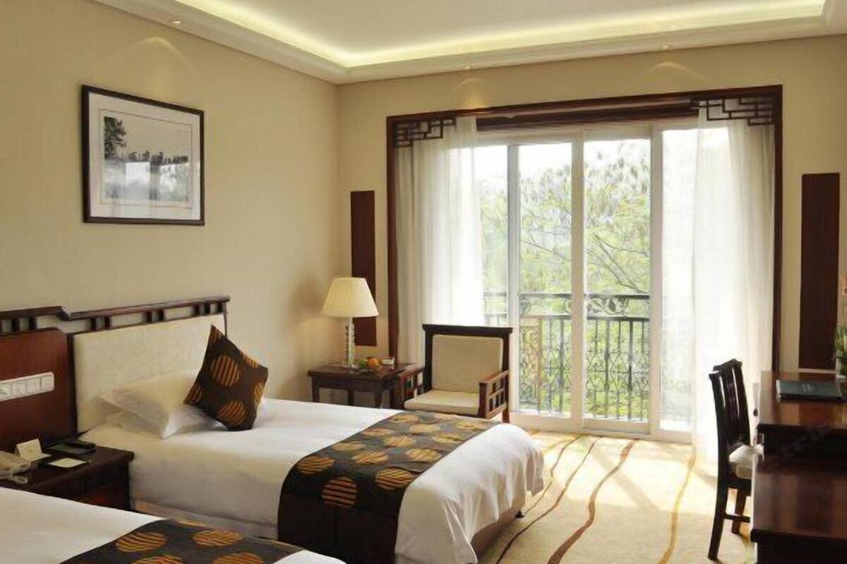Une chambre d’hôtel avec deux lits, un bureau, une chaise, une lampe et un balcon avec vue.