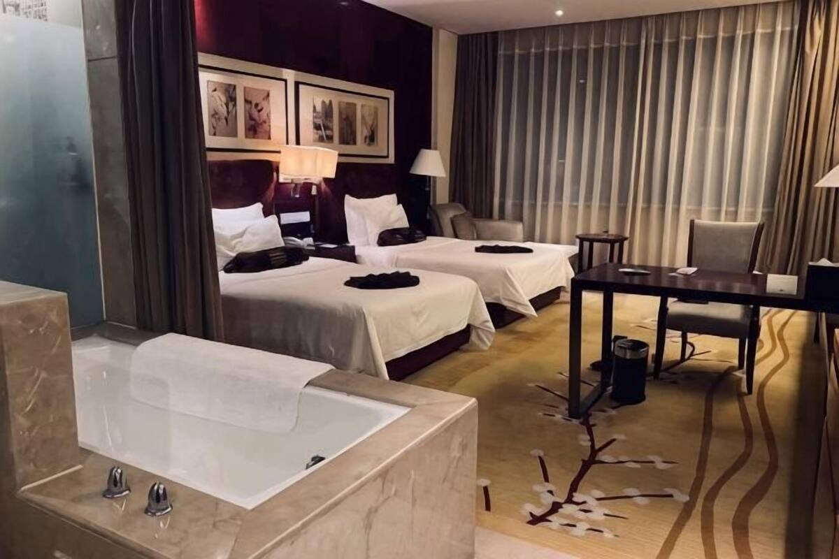 Une chambre d’hôtel avec une grande baignoire, deux lits, un bureau et une chaise.