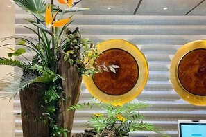 Un área de recepción con una planta grande, una columna de madera y un monitor de computadora sobre un escritorio.