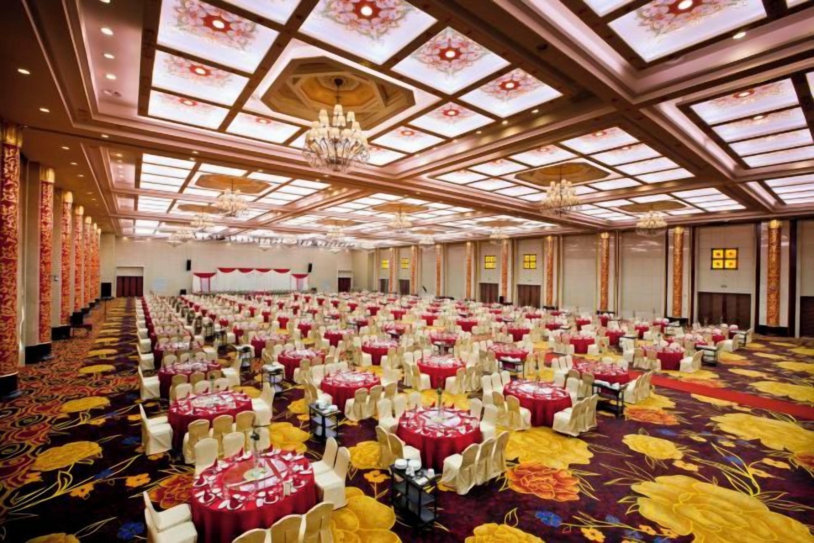 A banquet hall with rows of round tables, chandeliers, and a patterned carpet.