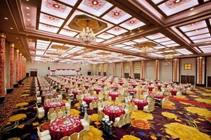 Un salón de banquetes con filas de mesas redondas, candelabros y una alfombra estampada.