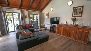 A spacious living room with a large sofa, wooden flooring, a television, and a wooden cabinet.