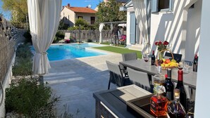 A poolside area with a table set for dining, a barbecue grill, and a variety of bottles.