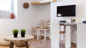 A compact kitchen with white cabinetry, a round dining table with two potted plants, and a TV mounted above the counter.