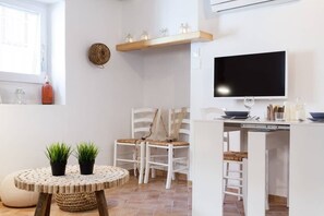 A compact kitchen with white cabinetry, a round dining table with two potted plants, and a TV mounted above the counter.