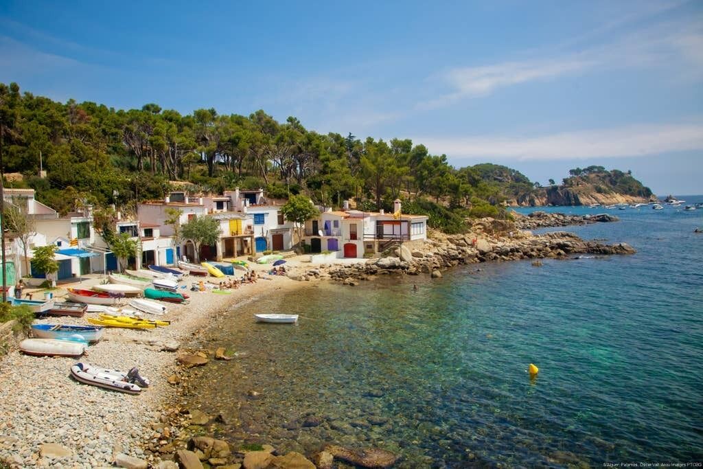 Un village côtier aux bâtiments aux couleurs vives, avec une plage de galets et des bateaux.