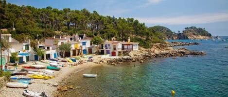 Un village côtier aux bâtiments aux couleurs vives, avec une plage de galets et des bateaux.