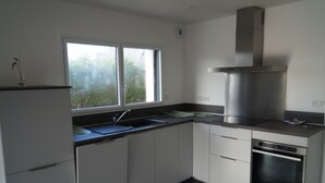 Una cocina moderna con gabinetes blancos, una campana extractora de acero inoxidable, un horno empotrado y una ventana con vistas a la vegetación.
