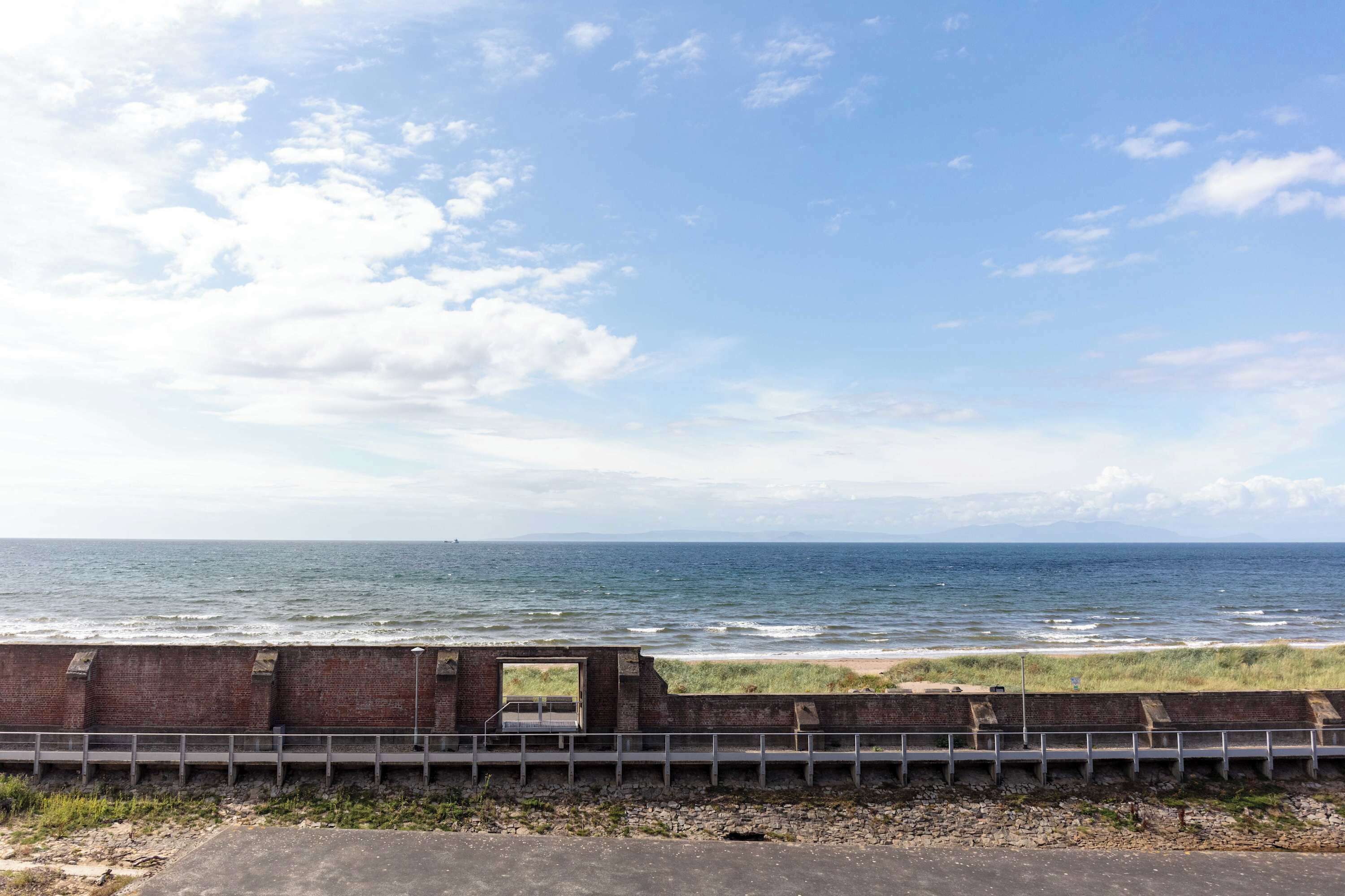 A coastal view with a brick wall and a metal railing.