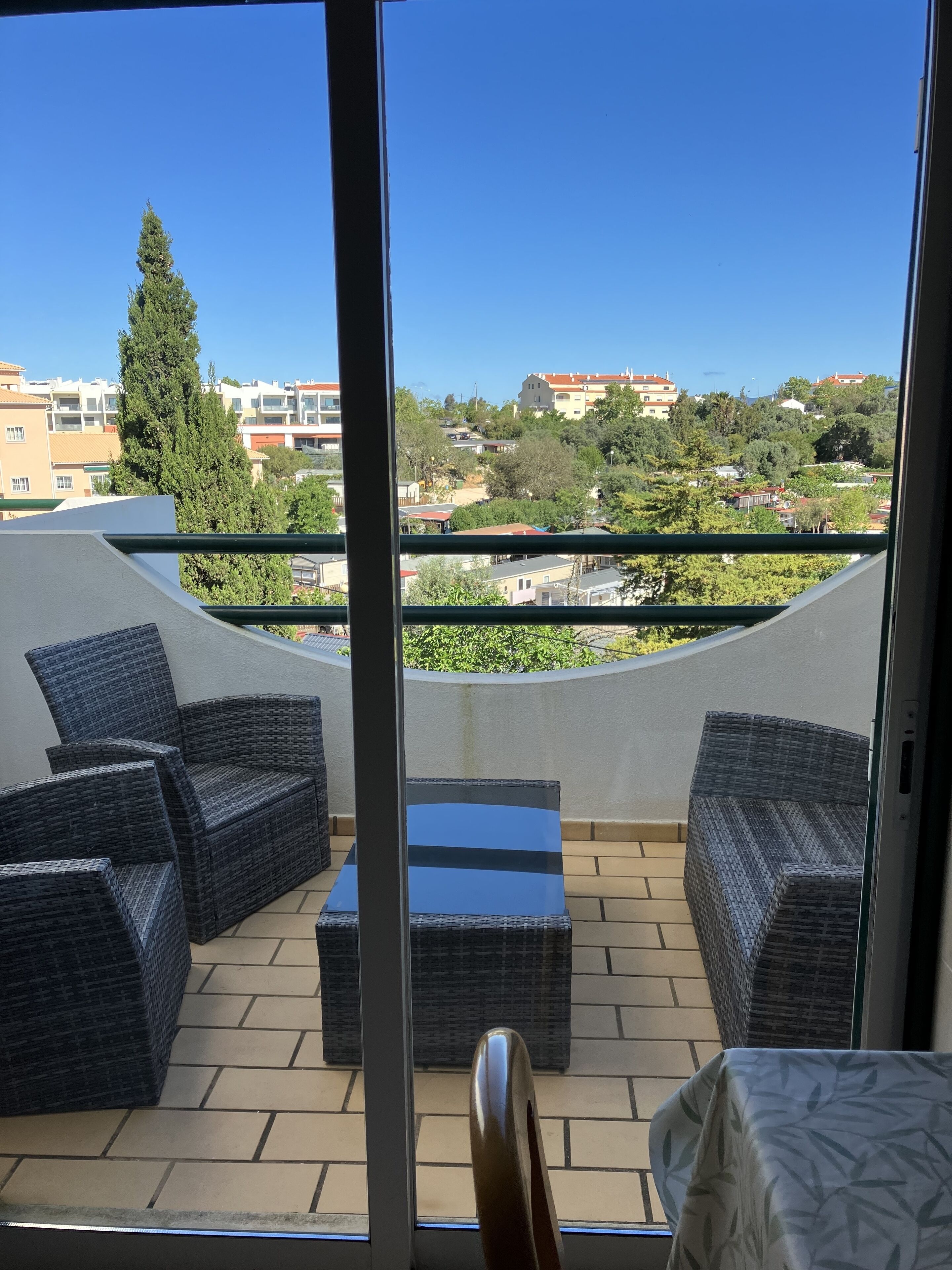 Ein Balkon mit Korbmöbeln, einer Glastür und Blick auf Gebäude und Bäume.