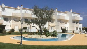 Um edifício com vários andares, varandas, piscina e um jardim bem cuidado.
