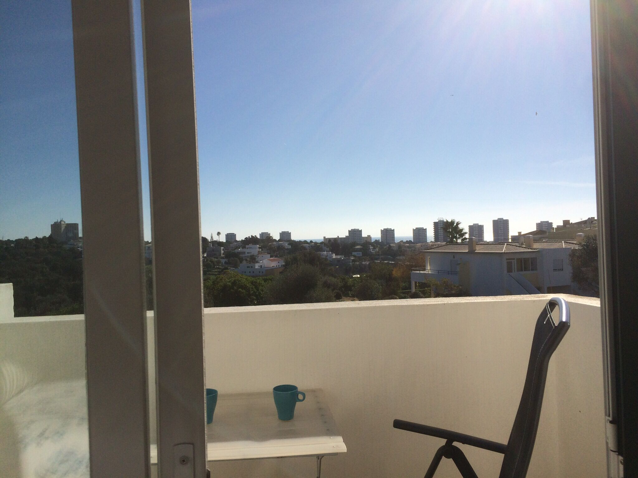 Un balcón con una mesa y dos sillas, con vistas a un paisaje urbano con edificios y zonas verdes.