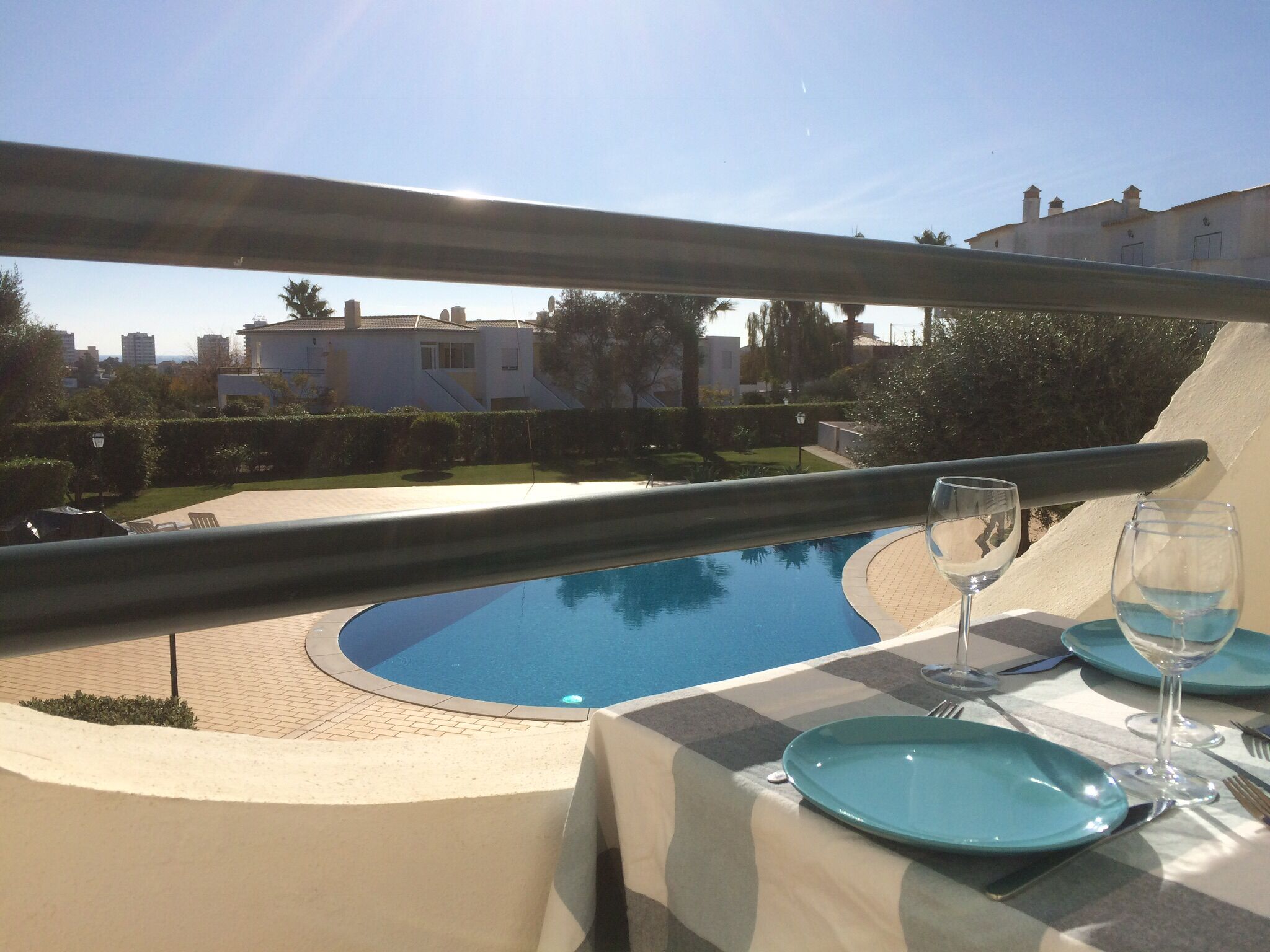 Ein Essbereich mit Blick auf einen Swimmingpool, ein Tisch gedeckt mit blauen Tellern und Weingläsern, und ein Geländer mit Aussicht auf eine Wohngegend.
