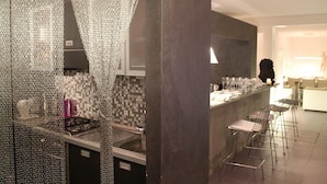 A modern kitchen with a stainless steel range hood, a tiled backsplash, and a bar area with stools.
