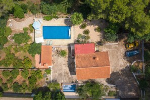 Ett flygbildsfoto av en fastighet med en swimmingpool, en byggnad med rött tak och en gul bil som står parkerad i närheten.