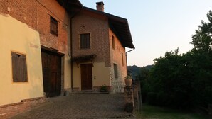 A two-story brick house with a cobblestone entrance, a wooden door, and a small garden with a potted plant.