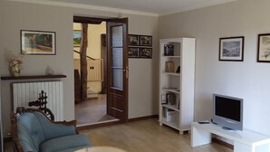 A living room with a sofa, a TV on a stand, a bookshelf, and a door leading to another room.