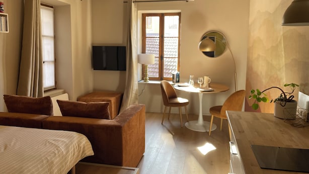 Ett hotellrum med en säng, en soffa, ett matbord med stolar, en tv som är monterad på väggen och ett fönster med gardiner.