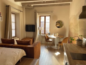 Een hotelkamer met een bed, een bank, een eettafel met stoelen, een aan de muur bevestigde televisie en een raam met gordijnen.