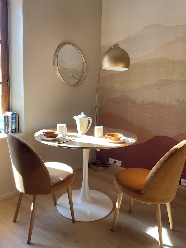 Een eetgedeelte met een ronde tafel, twee stoelen, een vloerlamp en een muur met een bergdecoratie.