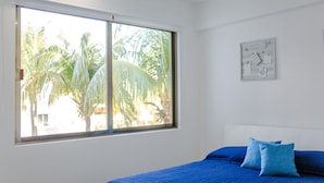 Un dormitorio con un ventanal grande, una cama con ropa de cama azul y un cuadro colgado en la pared.