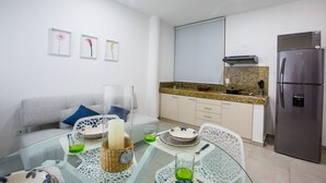 Una cocina moderna con refrigerador de acero inoxidable, encimera de granito y mesa de comedor de vidrio con sillas blancas.