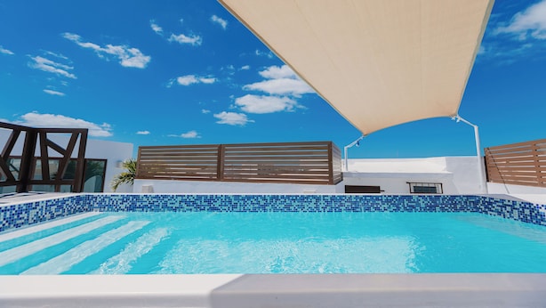 Una piscina con mosaicos azules, cerca viva de madera y un toldo grande.
