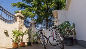 A gated courtyard with two bicycles parked against a wall, surrounded by potted plants and a stone wall. - Spacious villa with an outdoor swimming pool (Ðuraševici)