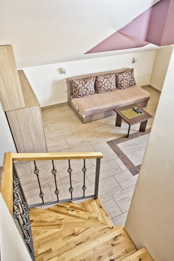 A staircase with wooden steps and metal balusters, leading to a living area with a sofa and a small table.