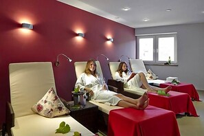 A spa room with individual treatment beds, each with a red table, a bottle, and a glass. - Weinberghotel Nalbach (Reil)