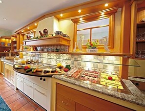 A kitchen with a buffet setup, a window with decorative items, and a tiled backsplash. - Weinberghotel Nalbach (Reil)