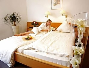 A hotel room with a bed, a bedside table, a lamp, a potted plant, and a vase with flowers.