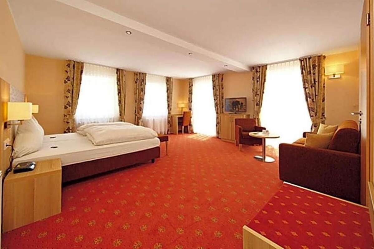 A hotel room with a bed, a sofa, a desk, and a chair.