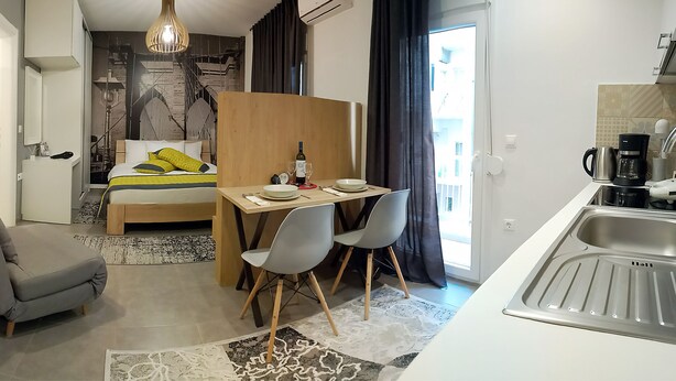 Une chambre d’hôtel compacte comprenant un lit, une petite table à manger avec des chaises, un coin cuisine et une vue sur la ville.