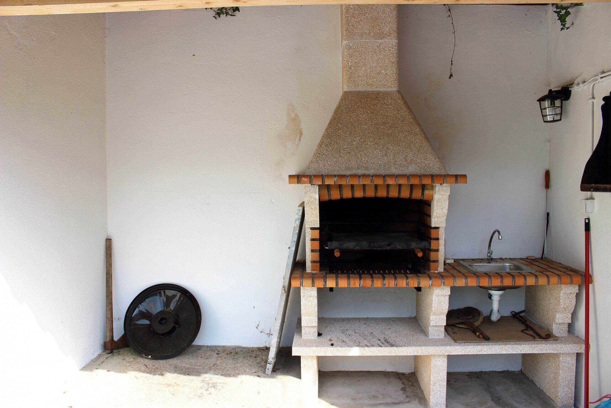 Un petit espace de cuisine extérieur comprenant un four en briques, un évier et un banc en bois.