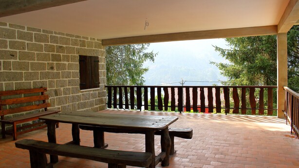 A covered patio with a picnic table and benches, stone walls, and a view of trees and mountains.