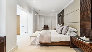 Een moderne slaapkamer met een groot bed, houten hoofdeinde en een bankje ernaast.