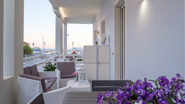 A modern outdoor seating area with a view of the sea, featuring a table, chairs, and a potted plant.