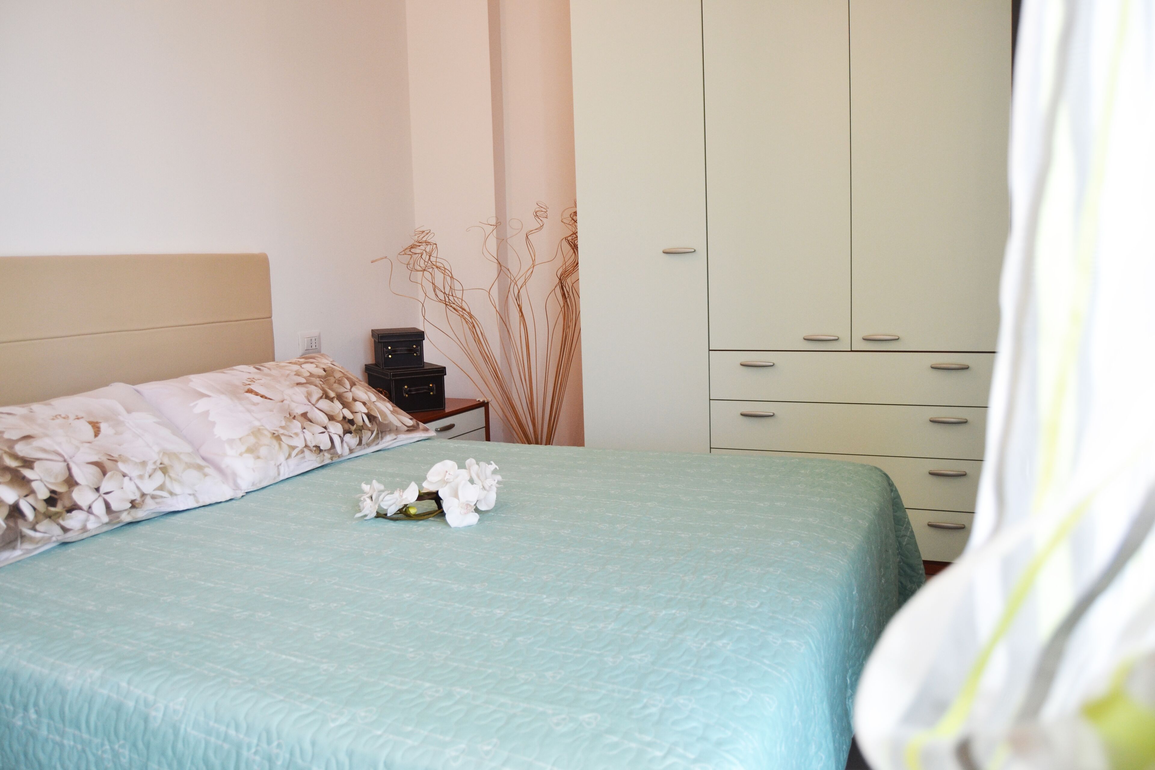 A bedroom with a bed, a nightstand, a wardrobe, and a decorative plant.