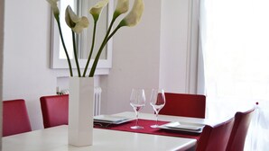 A dining table with a vase of white flowers, two empty wine glasses, and red chairs. - Apartment 100 meters from the beach (Gatteo A Mare)