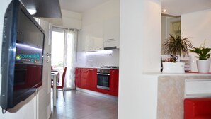 A modern kitchen with red and white cabinets, a built-in oven, and a dining area with a table and chairs. - Apartment 100 meters from the beach (Gatteo A Mare)